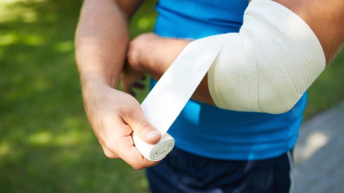 Man bandaging his injured arm Man bandaging his injured arm