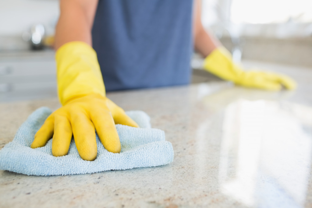 A person wearing yellow cleaning gloves while wiping a kitchen countertop