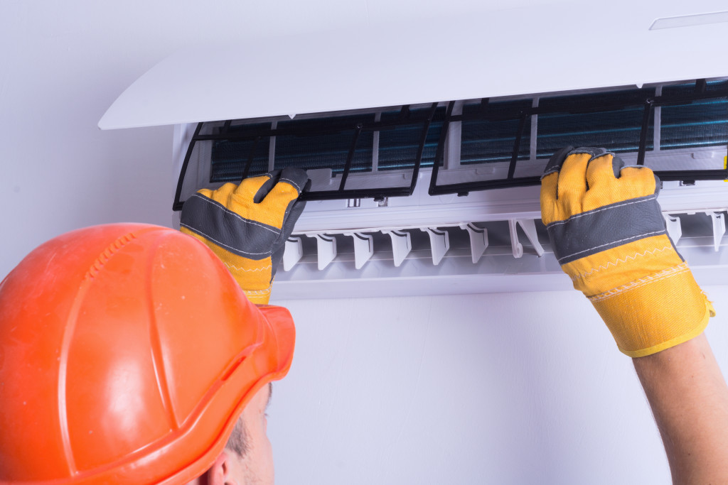 A worker with gloves and hardhat replacing the filters of an air conditioning unit